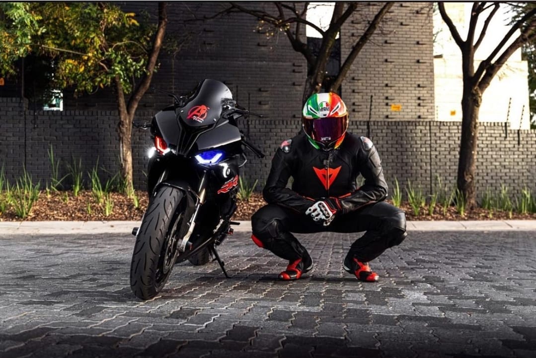 Alpha Team rider in leathers crouched beside a blacked-out BMW S1000RR