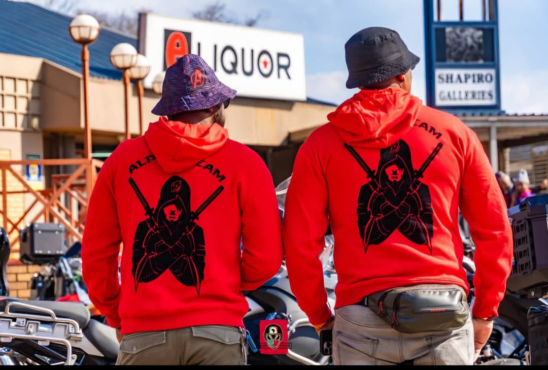 Two Alpha Team members in red club hoodies standing in front of parked motorcycles